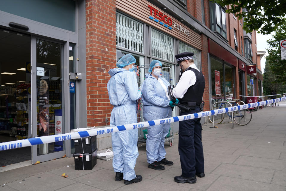 Police officers in forensic suits speak to a colleague outside Tesco Express on Fulham Palace Road, west London.