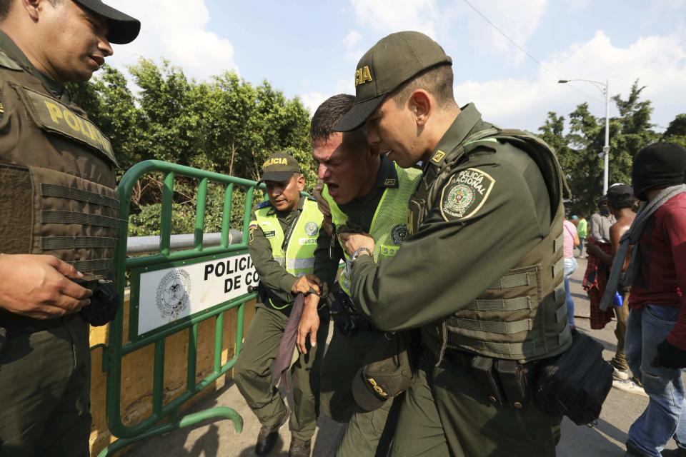 Colombian National Police help a fellow agent overcome by tear gas fired by Venezuelan National Guardsmen, who are blocking the entry of U.S.-supplied humanitarian aid on the Simon Bolivar International Bridge, during clashes with protesters in La Parada, Colombia, Monday, Feb. 25, 2019, on the border with Venezuela. Opponents of Venezuela President Nicolas Maduro clashed with Venezuelan security forces who are blocking the entry of U.S.-supplied humanitarian aid. (AP Photo/Fernando Vergara)