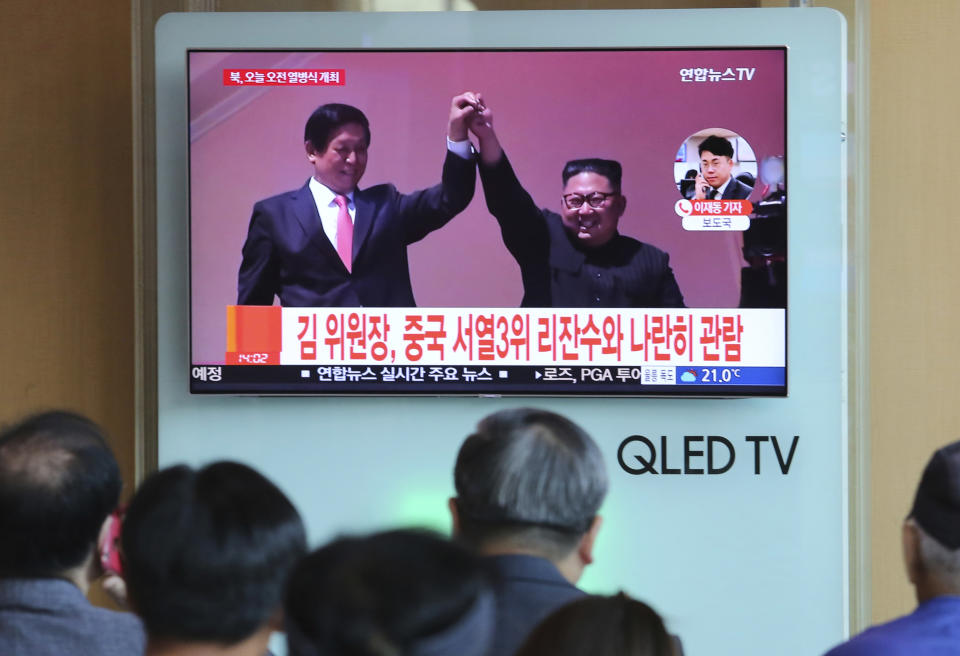 People watch a TV screen showing North Korean leader Kim Jong Un, right, raises hands with China's third-highest ranking official, Li Zhanshu, during a parade for the 70th anniversary of North Korea's founding day in Pyongyang, North Korea, during a news program at Seoul Railway Station in Seoul, South Korea, Sunday, Sept. 9, 2018. The signs read: " North Korean leader Kim Jong Un attends with China's third-highest ranking official, Li Zhanshu."(AP Photo/Ahn Young-joon)