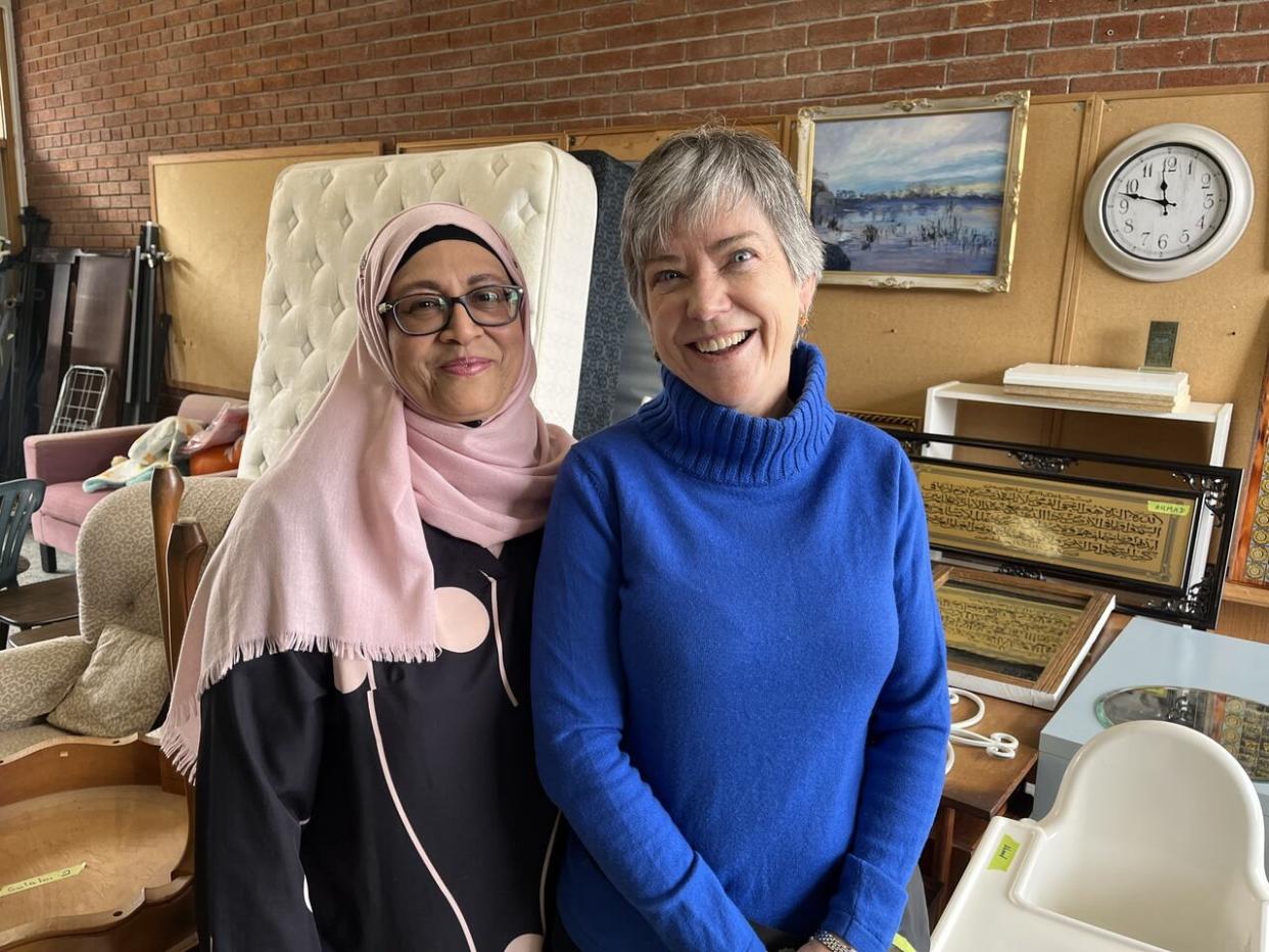 Amina Khote, left, the founder of Home Essentials Newcomer Support and Cathy Paterson, right, an organizer with the group, stand in front of some of the items available for new immigrants. They provide essential home supplies for free for newcomers in need. (Olivia Bowden/CBC - image credit)