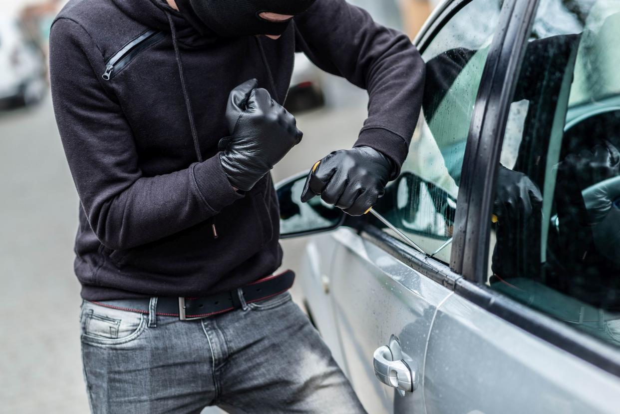 The man dressed in black with a balaclava on his head trying to break into the car. He uses a screwdriver. Car thief, car theft concept