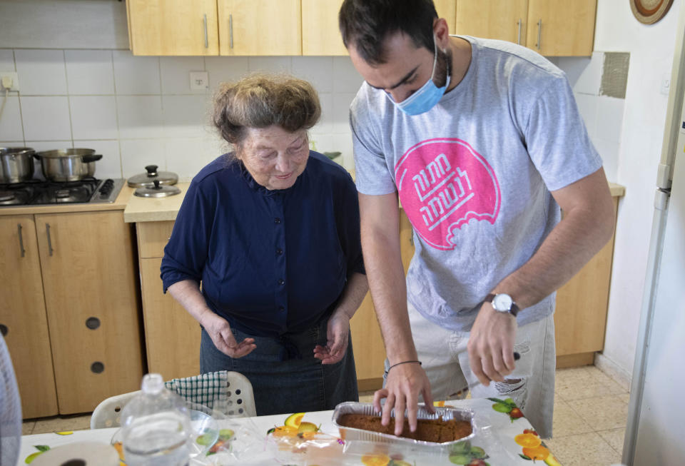 Sonia Rozenblatt, 85, tastes a cake made for her by Israeli volunteer Din Belz in the central Israeli city of Ra'anana, Thursday, Oct. 8, 2020. For thousands of older Israelis like Rozenblatt, being housebound alone during Israel's second nationwide lockdown due to the coronavirus pandemic is difficult and depressing. But each week ahead of the Jewish Sabbath, which starts on Friday at sundown, a home-baked cake is delivered by one of thousands of volunteers bringing pastries to home-bound older Israelis. (AP Photo/Sebastian Scheiner)