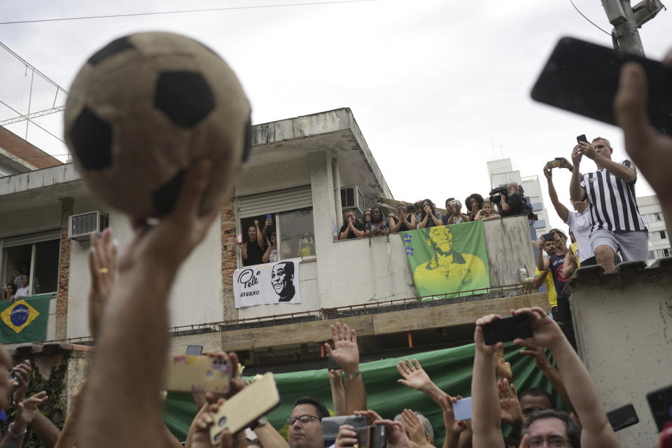 People watch the funeral procession of Brazilian soccer great Pele pass by the home of Pele's mother, where members of his family stand on the balcony, as his remains are taken from Vila Belmiro stadium to the cemetery in Santos, Brazil, Tuesday, Jan. 3, 2023. (AP Photo/Matias Delacroix)
