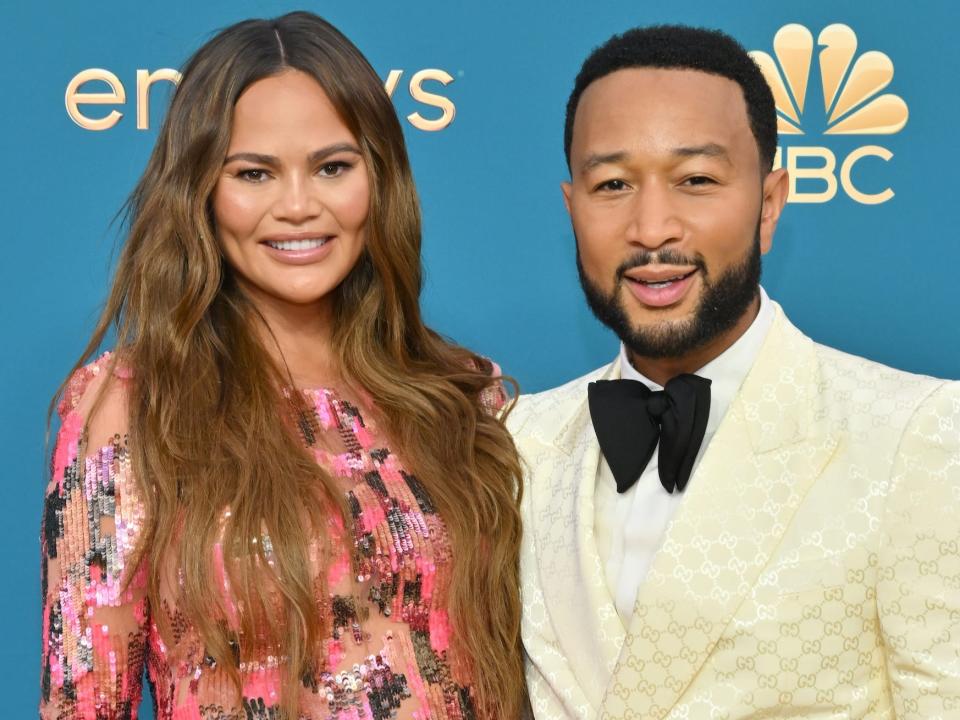 Chrissy Teigen, in a pink sparkly gown, poses with John Legend, in a cream suit and black bow tie, on the red carpet.