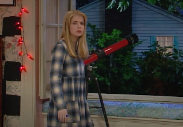 Character Clarissa from "Clarissa Explains It All" stands by a telescope, looking confused