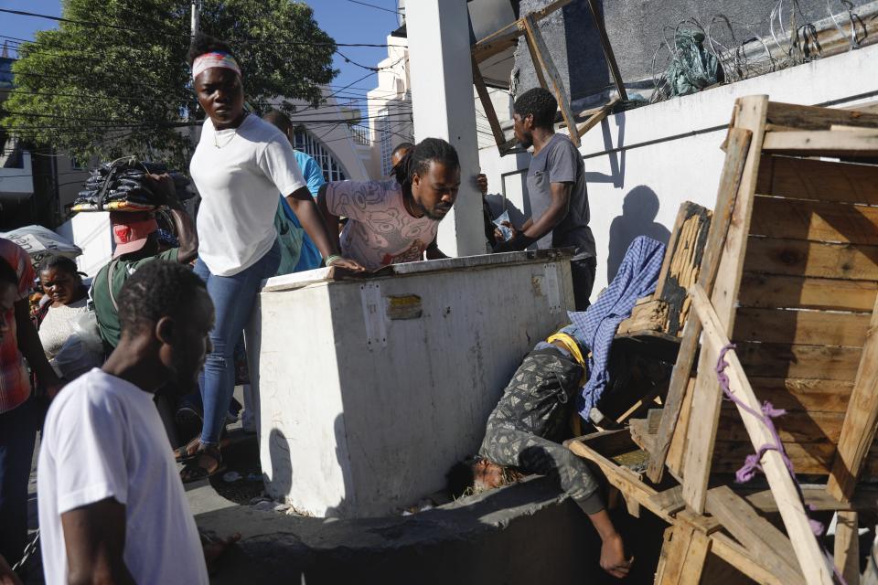 ARCHIVO - Un grupo de personas observa el cadáver de un hombre tras un tiroteo registrado durante la noche en el vecindario Petion Ville de Puerto Príncipe, Haití, el 18 de marzo de 2024. (AP Foto/Odelyn Joseph, archivo)