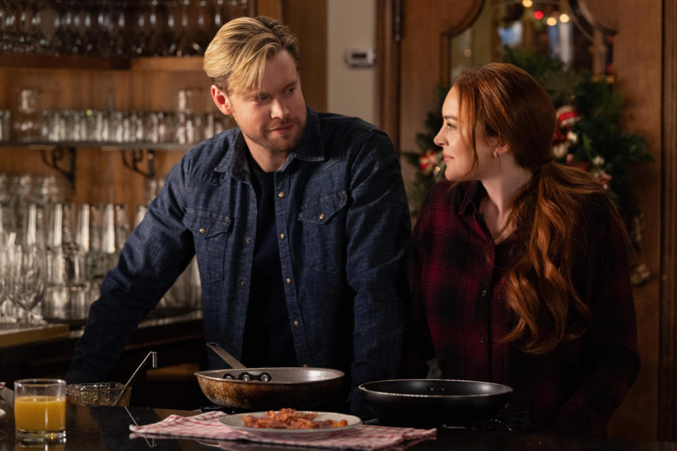 Overstreet with blond hair and a jean shirt looks to his left at lohan, who is in a red flannel. They're standing at a kitchne counter over pots and pans. (Scott Everett White / Netflix)