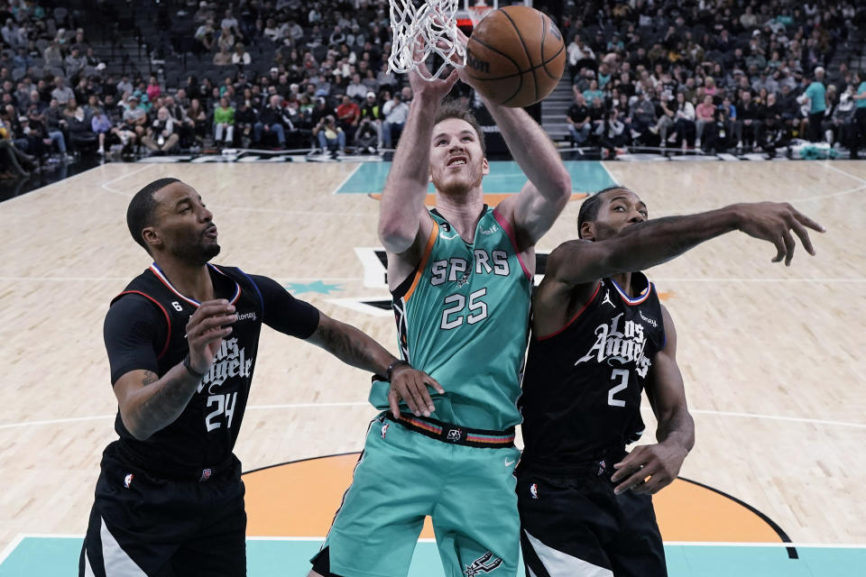 San Antonio Spurs center Jakob Poeltl (25) reaches between Los Angeles Clippers forward Norman Powell (24) and forward Kawhi Leonard (2) for a rebound during the first half of an NBA basketball game in San Antonio, Friday, Jan. 20, 2023. (AP Photo/Eric Gay)