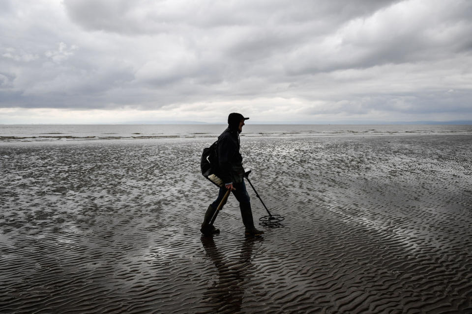 A man uses a metal detector on Barry Island beach, Wales.