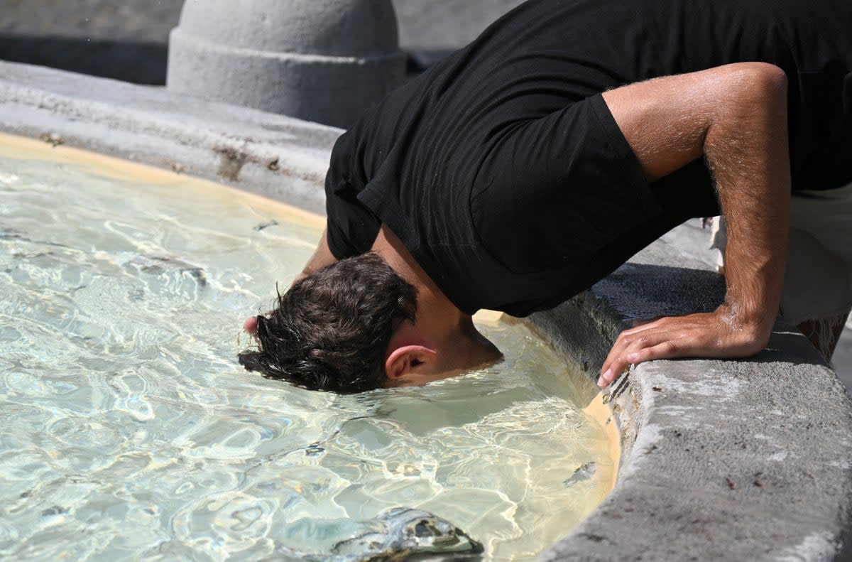 A man puts his head in the water to cool off at the fountain in Piazza del Popolo in Rome, on July 18, 2023 (Tiziana Fabi / AFP via Getty Images)