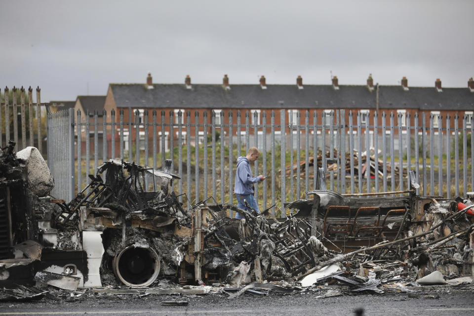 FILE - In this Thursday, April 8, 2021 file photo, a man walks past a burnt out bus on the Shankill road in West Belfast, Northern Ireland. The chaotic scenes during a week of violence on the streets of Northern Ireland have stirred memories of decades of Catholic-Protestant conflict, known as “The Troubles.” A 1998 peace deal ended large-scale violence but did not resolve Northern Ireland’s deep-rooted tensions. (AP Photo/Peter Morrison, File)