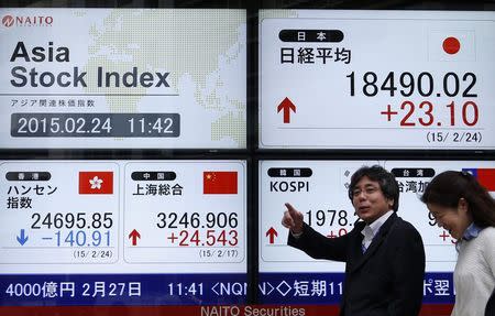 Pedestrians walk past an electronic board showing the stock market indices of various Asian countries outside a brokerage in Tokyo February 24, 2015. REUTERS/Yuya Shino