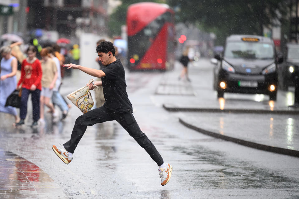 A man leaps over a puddle as shoppers rush through a heavy downpour in London.