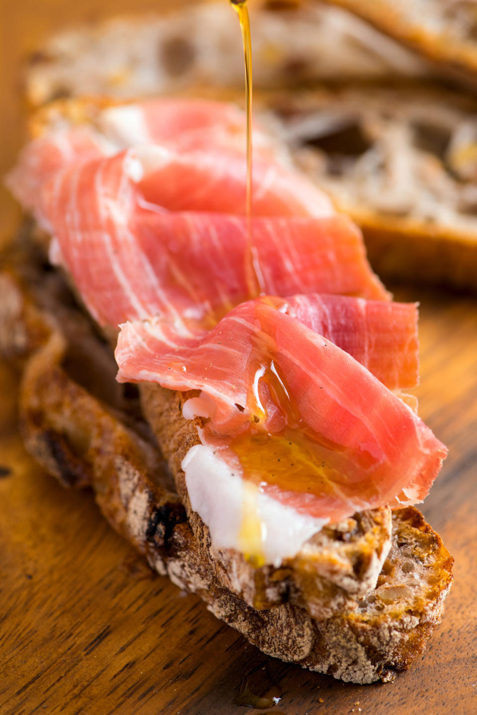 Drizzling olive oil on top of prosciutto and bread.