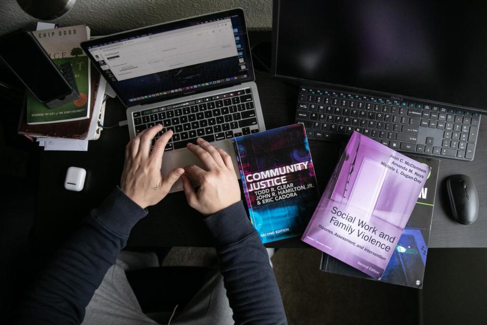 Two hands are on the keyboard of a laptop next to books and another computer.