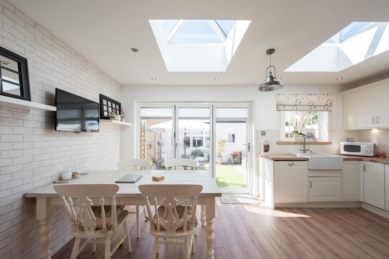 A general interior view of a cream beige shaker style fitted kitchen with, hardwood flooring, skylight, open-plan dining room diner, dining table and chairs with bi-fold patio doors