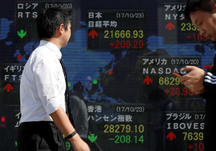 Passersby walk past an electronic board showing market indices outside a brokerage in Tokyo, Japan, October 23, 2017. REUTERS/Issei Kato