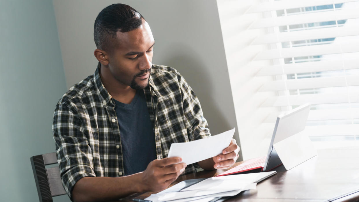 A young African-American man sitting at a table at home, paying bills.