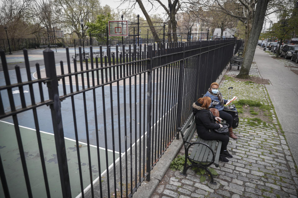 In this Thursday, April 23, 2020 photo, Ruth Caballero, a nurse with The Visiting Nurse Service of New York, right, and Catherine Peralta, her Spanish-language translator, sit next to an empty park as they have a teleconference with a patient during their rounds in upper Manhattan in New York. Home care nurses, aides and attendants, who normally help an estimated 12 million Americans with everything from bathing to IV medications, are now taking on the difficult and potentially dangerous task of caring for coronavirus patients. (AP Photo/John Minchillo)