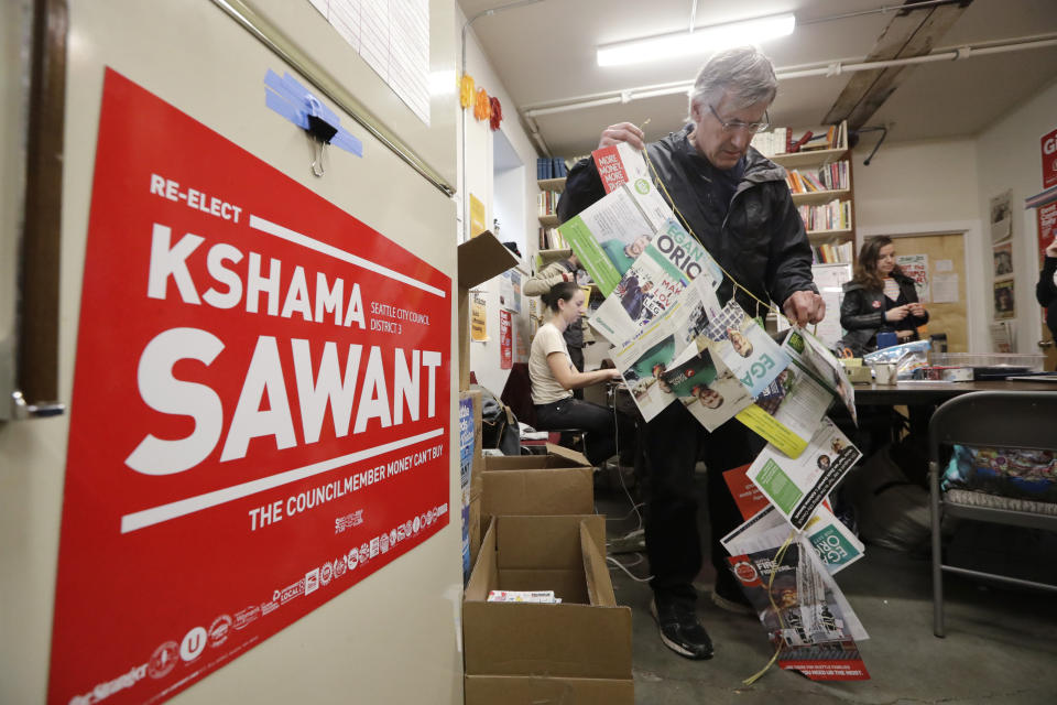 In this Wednesday, Oct. 23, 2019 photo, Merle Adler, a campaign volunteer for Seattle City Council candidate Kshama Sawant, unfurls a string of mailings he received at home in support of challenger Egan Orion, at the campaign office in Seattle. Adler brought the mailings to show Sawant campaign workers how much money and effort is going into the campaign of Orion. Seven of the nine Seattle City Council seats are up for grabs in next month's election, where retail giant Amazon has made unprecedented donations totaling $1.5 million to a political action committee that's supporting a slate of candidates perceived to be friendlier to business. Among the company's top targets is Sawant, a fierce critic of Amazon, who is running against Orion in the District 3 race. (AP Photo/Elaine Thompson)
