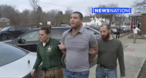 This image taken from video provided by Newsnation/TMX shows reporter Evan Lambert being taken into police custody on Wednesday, Feb. 8, 2023 in East Palestine, Ohio. NewsNation posted video of their correspondent being arrested Wednesday in the gymnasium of an elementary school in East Palestine where Gov. Mike DeWine was giving an update about the accident. Lambert was held for about five hours before being released from jail, NewsNation reported.(Newsnation TMX via AP)