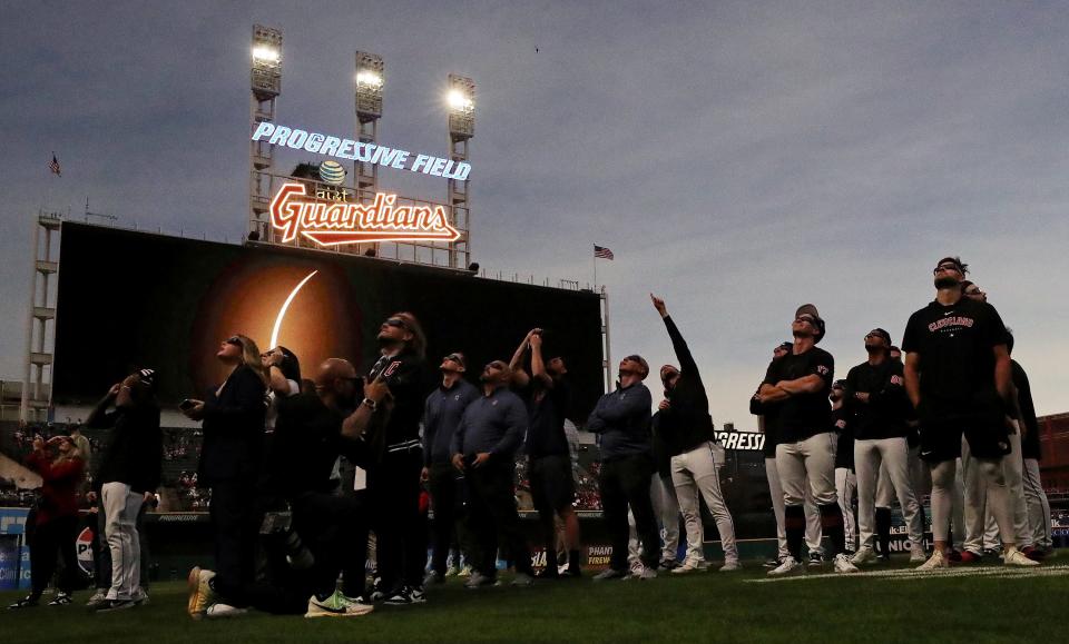 Cleveland Guardians staff and players stand on the third base line to watch as the solar eclipse nears totality at Progressive Field before the Cleveland Guardians' home opener against the Chicago White Sox Monday.