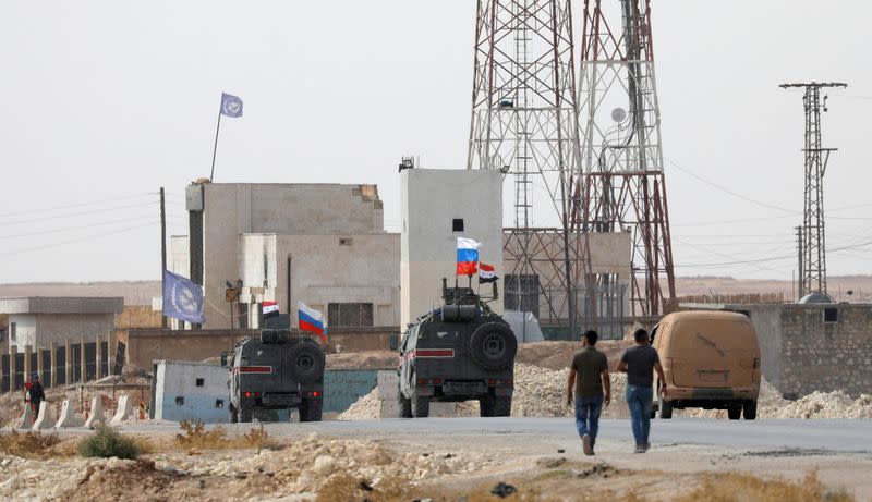 FILE PHOTO: Russian and Syrian national flags flutter on military vehicles near Manbij