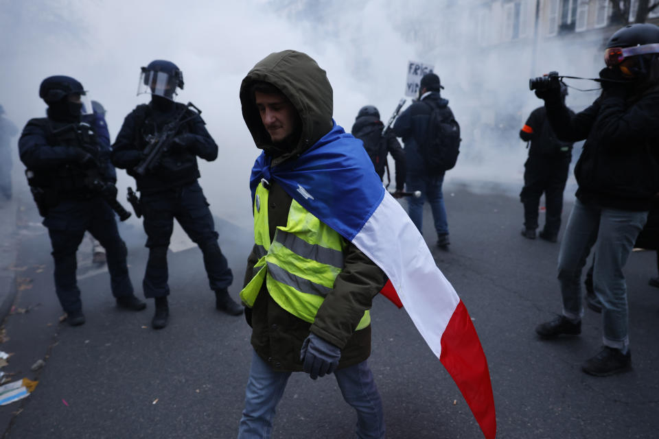 A demonstrator walks past riot police officers during a demonstration against pension changes, Thursday, Jan. 19, 2023 in Paris. Workers in many French cities took to the streets Thursday to reject proposed pension changes that would push back the retirement age, amid a day of nationwide strikes and protests seen as a major test for Emmanuel Macron and his presidency. (AP Photo/Lewis Joly)