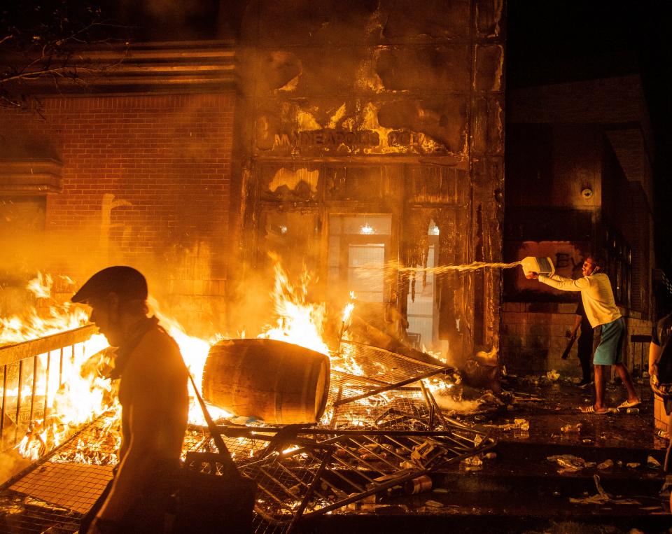 A protester dumps heating fuel on the fire at the Minneapolis Police 3rd precinct Thursday, May 28, 2020. Protests continued around the city following the death of George Floyd, a black man who died in police custody.