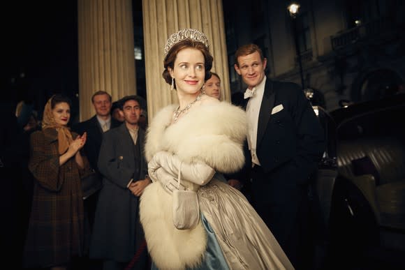 A woman wearing a crown and a man in a tuxedo smiling in a scene from Netflix's The Crown starring Claire Foy and Matt Smith.