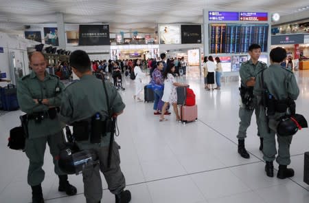 Passengers walk next to riot police inside Hong Kong International Airport in Hong Kong, China