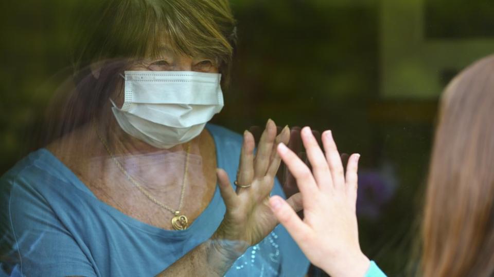 Abuela saludando a su nieta detrás de una ventana