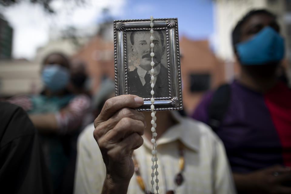 En esta imagen, tomada el 26 de octubre de 2020, una devota sostiene una imagen enmarcada del fallecido doctor José Gregorio Hernández en el exterior de la iglesia de La Candelaria donde están enterrados sus restos, en Caracas, Venezuela. Los restos de Hernández, conocido popularmente como el "doctor de los pobres", fueron exhumados el lunes en una ceremonia a puerta cerrada en la iglesia del centro de Caraca como parte de las exigencias del Vaticano para la beatificación del primer laico venezolano. (AP Foto/Ariana Cubillos)