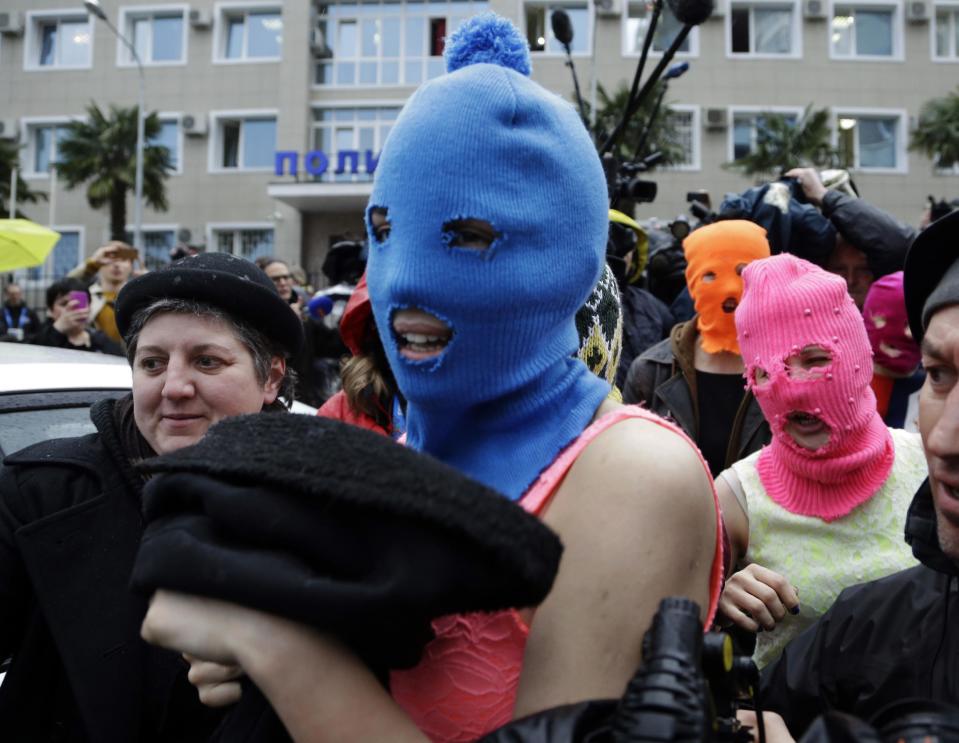 Russian punk group Pussy Riot members Nadezhda Tolokonnikova, in the blue balaclava, and Maria Alekhina, in the pink balaclava, make their way through a crowd after they were released from a police station, Tuesday, Feb. 18, 2014, in Adler, Russia. No charges were filed against Tolokonnikova and Alekhina along with the three others who were held. (AP Photo/Morry Gash)