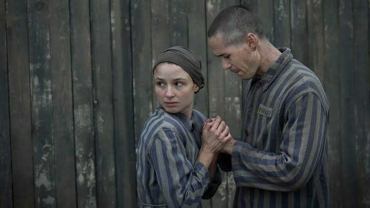 A man holds a woman's hands, she looks to the left away from him in a scene from The Tattooist of Auschwitz.