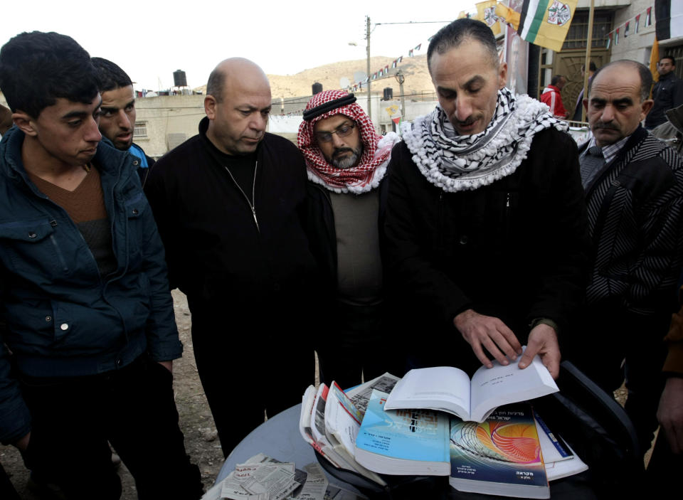 In this Friday, Jan. 3, 2014 photo, Jamal Abu Muhsin, second right, who is among hundreds of Palestinians having spent their time in Israeli prisons pursuing an education and was recently released, shows books he studied from to earn his university degree at an Israeli prison in the West Bank town of Tubas near Jenin. Abu Muhsin spent his time in prison pursuing an education _ a program that has been praised by Palestinians but has caused a stir with Israelis who believe that murderers are being undeservedly coddled. "When I found myself in jail for life, I was faced with two options: either I make meaning for my life or waste my life and my mind behind bars," said Abu Muhsin, now 42, from his home in the West Bank city of Tubas. (AP Photo/Nasser Ishtayeh)