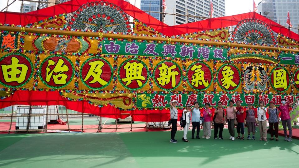 香港維多利亞公園足球場上一群長者在親建制團體慶祝「七一」活動的「由治及興」大型花牌前拍照留念（30/6/2023）