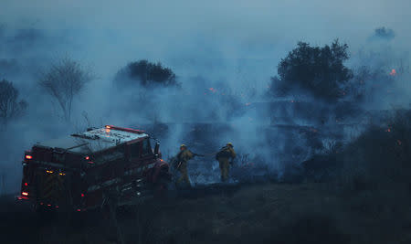 Firefighters sprays water on the Lilac Fire, a fast moving wildfire in Bonsall, California, U.S., December 7, 2017. REUTERS/Mike Blake