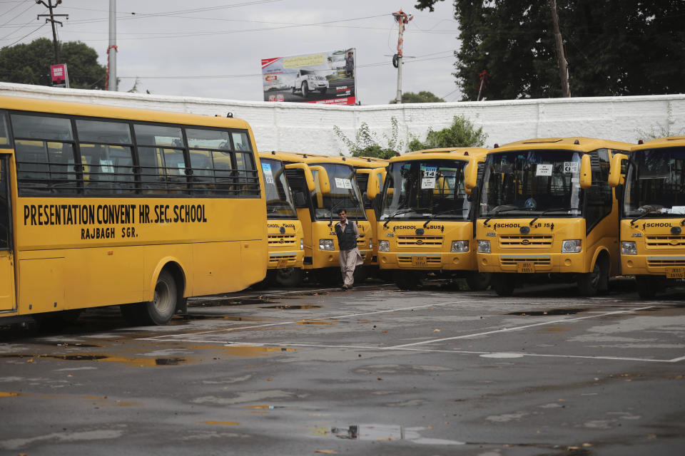 A staff member walks near buses parked inside the premises of a deserted school compound in Srinagar, Indian controlled Kashmir, Monday, Aug. 19, 2019. Restrictions continue in much of Indian-administered Kashmir, despite India's government saying it was gradually restoring phone lines and easing a security lockdown that's been in place for nearly two weeks. (AP Photo/Mukhtar Khan)