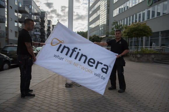 Two people on a sidewalk holding a sign with the Infinera logo and slogan.