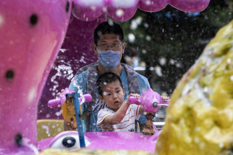 A man wearing a mask to curb the spread of the new coronavirus and a child who temporarily removed his to enjoy a ride at a local park in Beijing on Saturday, May 23, 2020. New coronavirus cases dropped to zero in China for the first time Saturday but overwhelmed hospitals across Latin America – both in countries lax about lockdowns and those lauded for firm, early confinement. (AP Photo/Ng Han Guan)