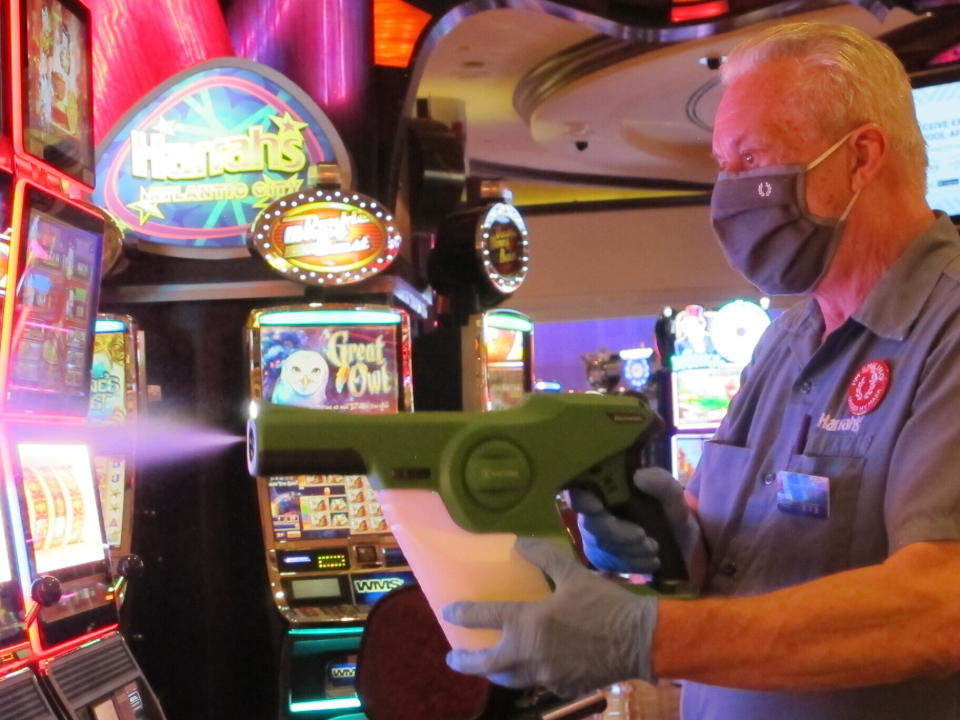 Steven Ford, a worker at Harrah's casino in Atlantic City, N.J., sprays slot machines with disinfectant Wednesday, July 1, 2020, as the casino prepared to reopen after 3 1/2 months of being shut down due to the coronavirus. Five of Atlantic City's casinos will reopen on Thursday, while three others, including Harrah's, will open Friday. (AP Photo/Wayne Parry)