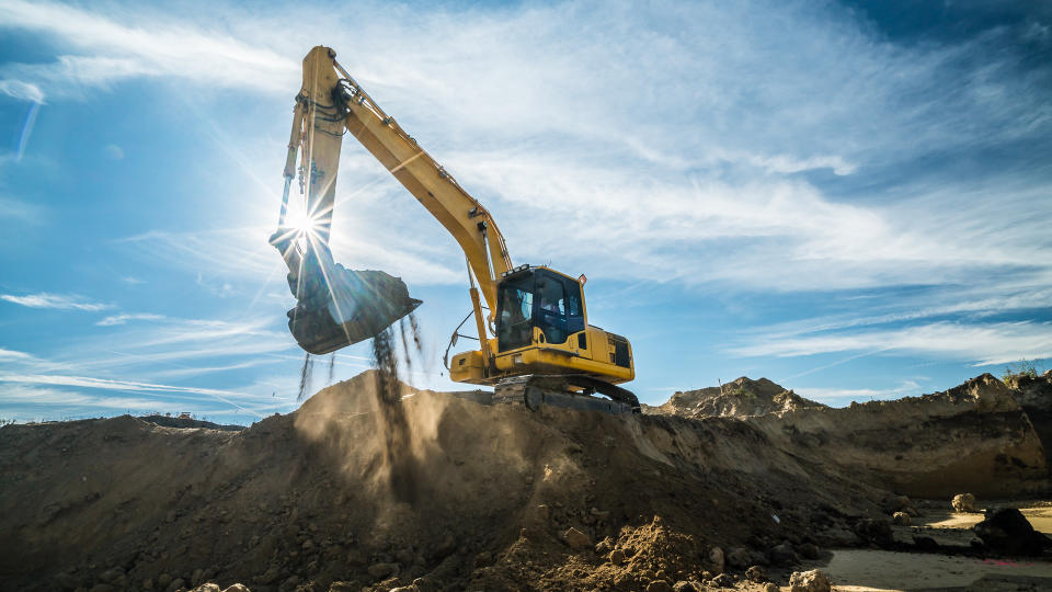 yellow digger digging excavation for new houses on a building site in backlight, high noise from recoverd shadows.