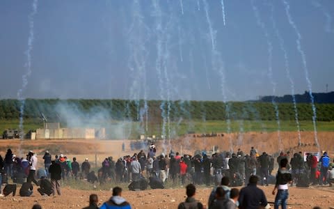 Teargas canisters fired by Israeli troops fall down on Palestinians during a demonstration near the Gaza Strip border - Credit: AP Photo/Khalil Hamra