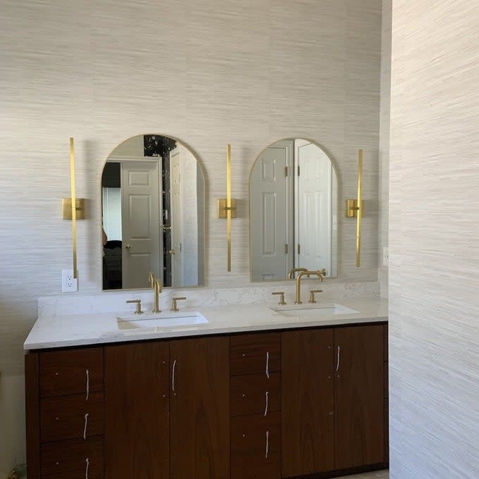 Bathroom with double vanity, arched mirrors, and gold fixtures