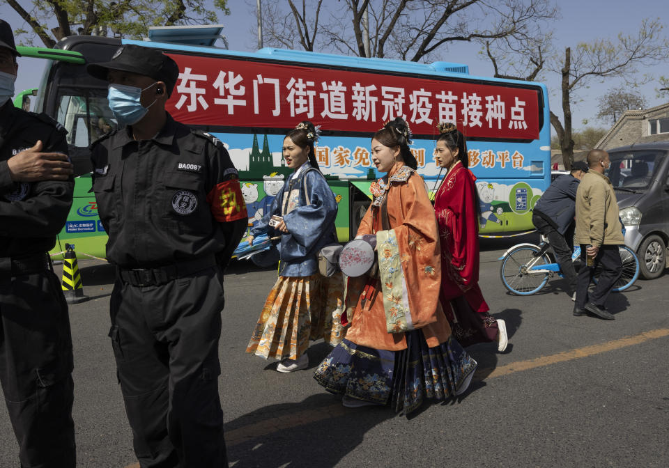 Residents in traditional costumes pass a bus offering free coronavirus vaccinations at an entrance to the Forbidden City in Beijing on Wednesday, April 14, 2021. China's success at controlling the outbreak has resulted in a population that has seemed almost reluctant to get vaccinated. Now it is accelerating its inoculation campaign by offering incentives — free eggs, store coupons and discounts on groceries and merchandise — to those getting a shot. ​(AP Photo/Ng Han Guan)