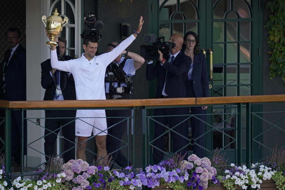 Serbia's Novak Djokovic holds the winners trophy to show to fans gathered outside Centre Court as he celebrates after beating Australia's Nick Kyrgios to win the final of the men's singles on day fourteen of the Wimbledon tennis championships in London, Sunday, July 10, 2022. (AP Photo/Alberto Pezzali)