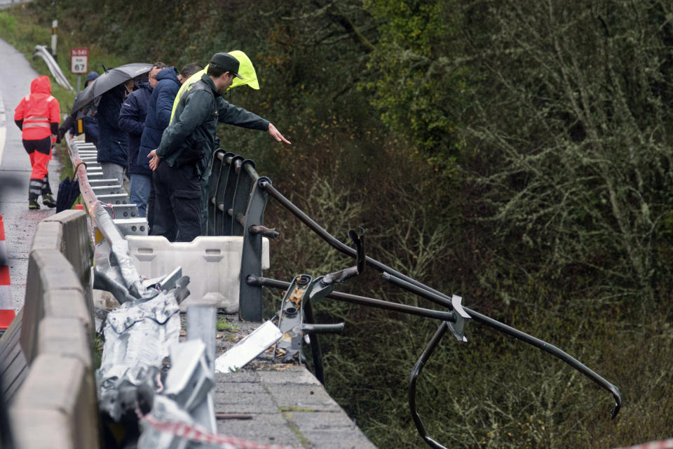 A civil guard points toward a bus after it plunged into a river near Pontevedra in northwestern Spain, Sunday, Dec. 25, 2022. Authorities say rescuers have recovered the victims from the bus that ran off a bridge and plunged into the river on Christmas Eve, killing six passengers and injuring the driver and another passenger. The Spanish Guardia Civil says a total of eight people were on the bus. The two survivors were rescued Saturday night and taken to hospitals. The bodies of the dead were retrieved Sunday. (Cesar Arxina/Europa Press via AP)