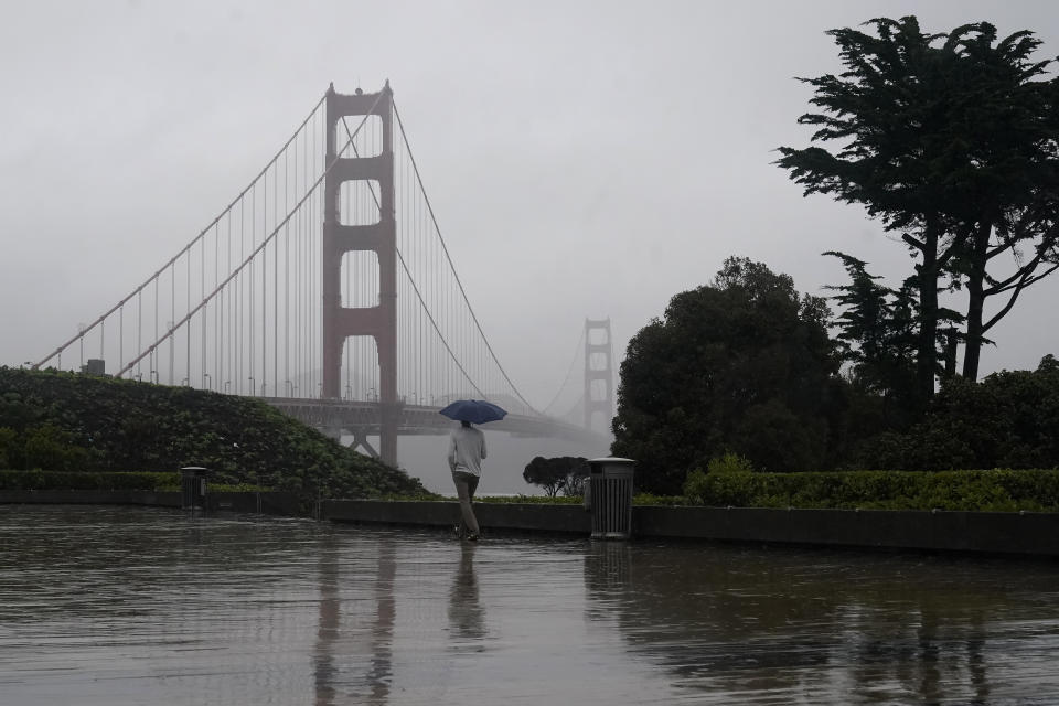 A pedestrian carries an umbrella while walking toward a path in front of the Golden Gate Bridge in San Francisco, Wednesday, Jan. 11, 2023. (AP Photo/Jeff Chiu)