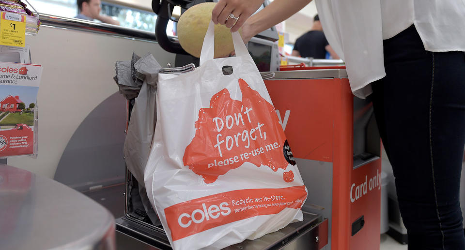 A woman uses a reusable Coles plastic bag at a self checkout.